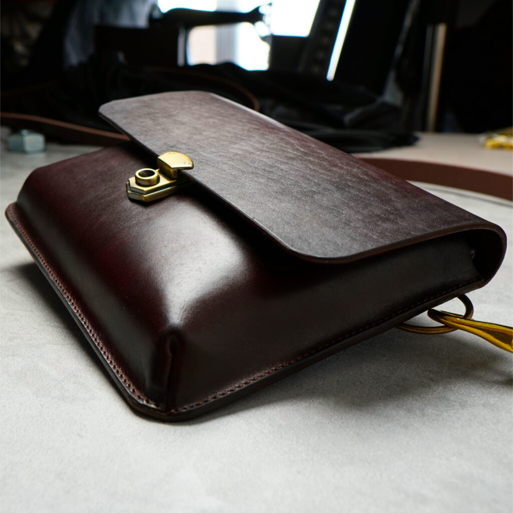chestnut colour leather crossbody bag laying on concrete with blurry background